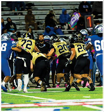 Several people in football uniforms are engaged in a play on a brightly lit field with spectators in the background. Description generated by AI