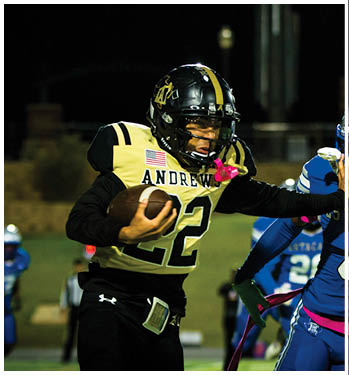 Two people in football uniforms are engaged in a play on a field at night, with one holding the ball and the other reaching out to block or tackle. Description generated by AI