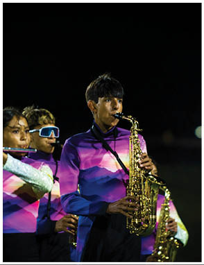 People wearing colorful uniforms are playing saxophones and flutes in a nighttime outdoor band performance. Description generated by AI