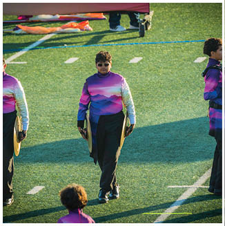 People wearing colorful gradient uniforms are standing on a field holding musical instruments, likely participating in a marching band performance. Description generated by AI