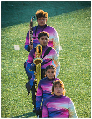 Two people wearing matching purple and white band uniforms are standing outdoors, one holding a saxophone and the other holding a clarinet. Description generated by AI