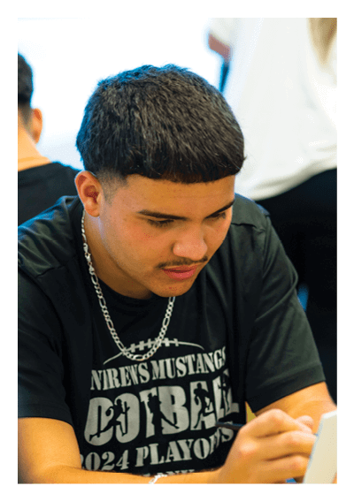 A person with short hair wearing a black sports t-shirt and a chain necklace is focused on writing or drawing on a surface in front of them. Description generated by AI