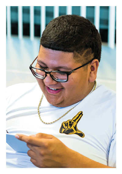 A person wearing glasses and a white shirt with a gold chain is smiling while holding and using a stylus on a tablet. Description generated by AI