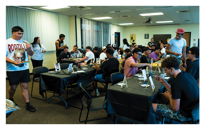 People gathered in a room sitting at tables covered with black tablecloths, engaging in activities involving small easels and art supplies. Description generated by AI