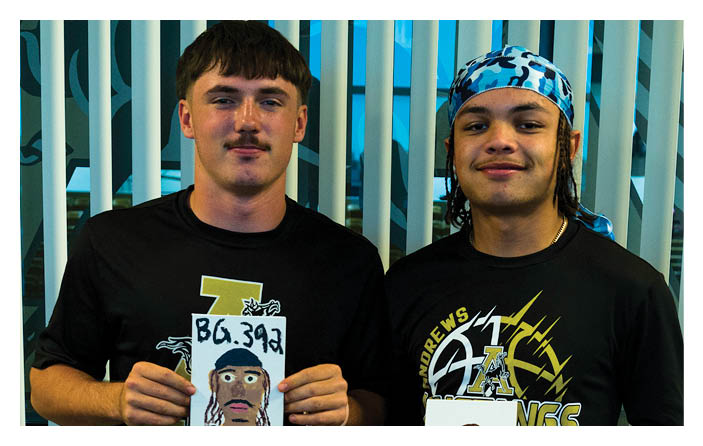 Two adults stand side by side in front of vertical blinds with one wearing a black shirt and the other wearing a black shirt and a blue patterned headscarf. Description generated by AI