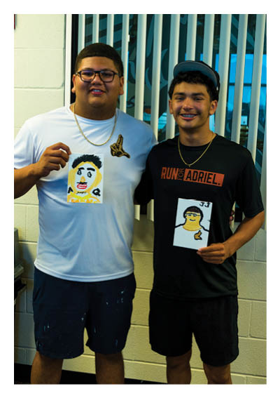 Two people wearing glasses and necklaces stand close together smiling in front of vertical blinds. Description generated by AI