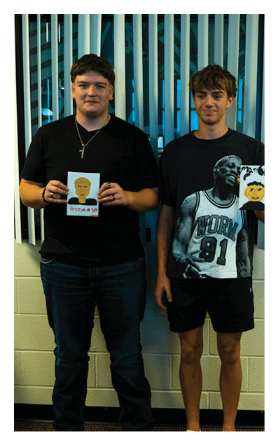 Two adults stand side by side indoors holding small portraits, one wearing a black shirt and jeans and the other wearing a black graphic t-shirt, shorts, and sandals. Description generated by AI