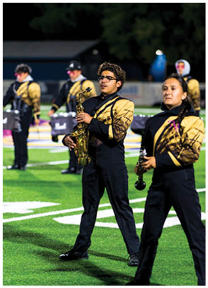 People in matching uniforms are playing musical instruments on a football field during a nighttime performance. Description generated by AI