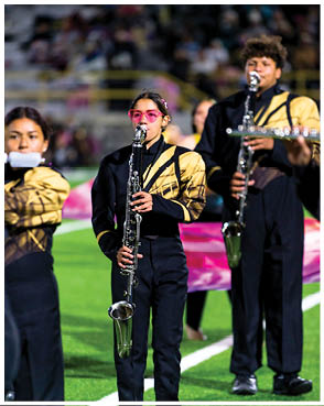 People in matching black and gold uniforms are playing clarinets on a sports field with a blurred crowd in the background. Description generated by AI
