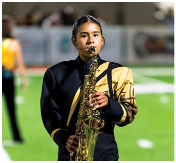 A person wearing a black and yellow marching band uniform is playing a saxophone on a field. Description generated by AI