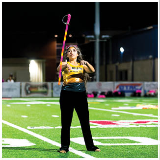 A person wearing a yellow shirt and black pants is standing on a sports field at night, holding a colorful ring toss stick. Description generated by AI