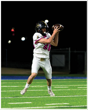 A person wearing a blue sports jersey with the number three and white pants is running on a green football field at night. Description generated by AI