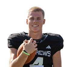 A person wearing a black football uniform with the number four is standing on a field holding a football and smiling. Description generated by AI