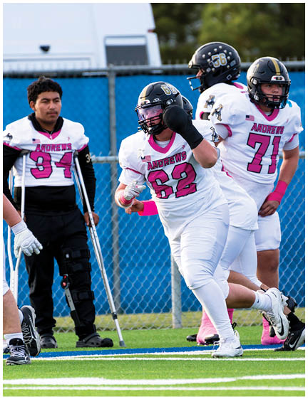 Three people in football uniforms are on a field, with one person running while holding a football, another standing with crutches and a leg brace, and the third standing nearby. Description generated by AI