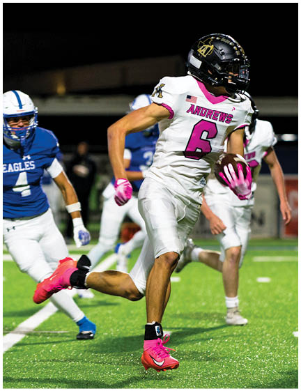 Two people in white football uniforms with pink accents are running on a field while a person in a blue uniform chases them during a nighttime game. Description generated by AI