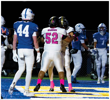 People wearing sports uniforms and bright pink socks are standing on a blue and yellow field, likely during a football game. Description generated by AI