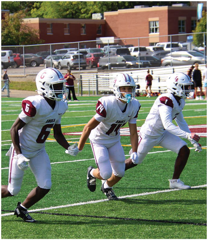 Three football players in blue and white uniforms running on a field. Description generated by AI