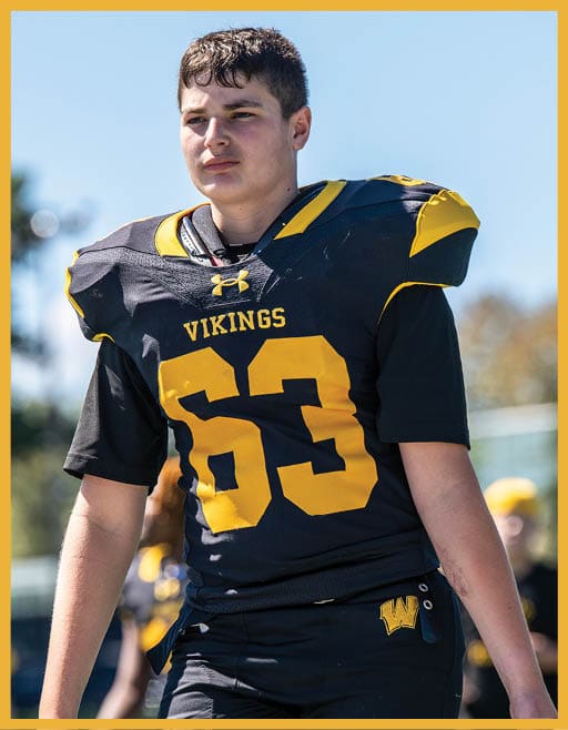 A person wearing a black and yellow Vikings football uniform with the number 63 stands outdoors on a sunny day. Description generated by AI
