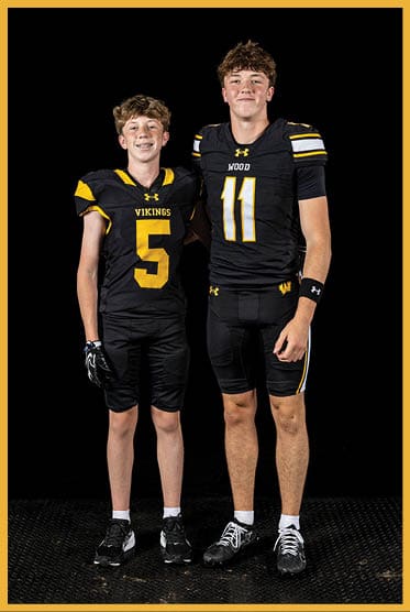 Two people wearing black and yellow football uniforms with numbers five and eleven stand side by side against a black background. Description generated by AI