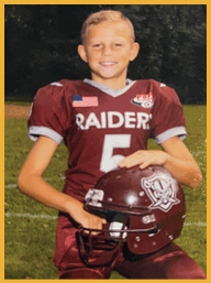 A child wearing a maroon football jersey with an American flag patch is smiling outdoors at night. Description generated by AI
