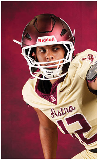 A person wearing a maroon and cream football uniform with the number 13 and a maroon helmet is leaning forward against a maroon background. Description generated by AI