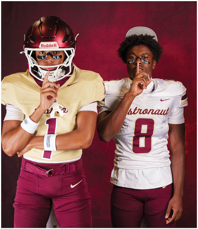 Three people wearing football uniforms stand against a dark red background, each holding a finger to their lips in a shushing gesture. Description generated by AI