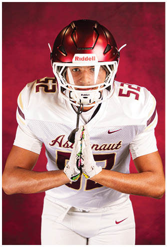 A person wearing a white football uniform with the number 52 and a red helmet is standing with hands pressed together in front of a red background. Description generated by AI