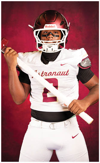 A person wearing a football helmet and jersey holds a white football bat against a red background. Description generated by AI