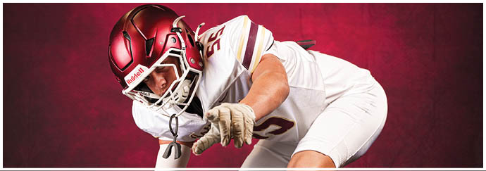A person in a white football uniform and red helmet is crouched forward against a red background. Description generated by AI