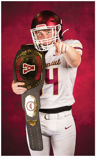A person wearing a football helmet and jersey is holding a championship belt with the words “Battle for the Belt" and a large letter A on it against a red background. Description generated by AI
