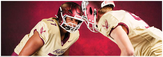 Two people wearing football helmets and uniforms are facing each other in a ready stance against a red background. Description generated by AI