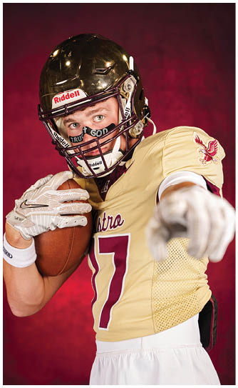 A person wearing a football helmet and uniform is holding a football and pointing forward against a red background. Description generated by AI