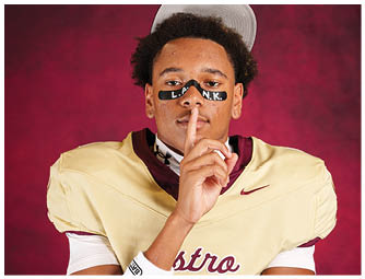 A person wearing a sports jersey and cap holds a finger to their lips with black face paint under their eyes spelling “L.A.N.K." against a red background. Description generated by AI