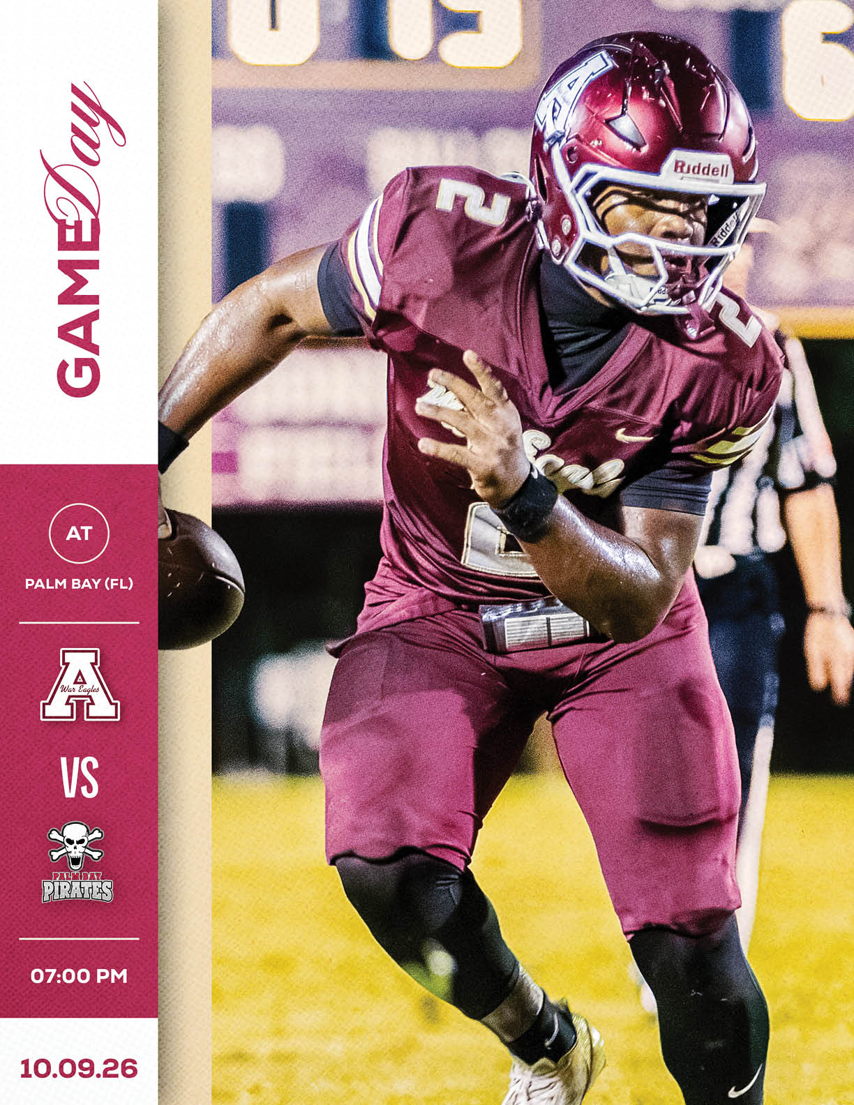 An adult in a maroon football uniform and helmet is running with a football on a field during a game, with a scoreboard and referee visible in the background. Description generated by AI