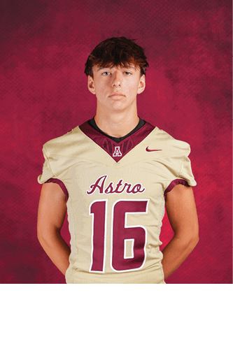 A person with short tousled hair stands against a red textured background wearing a beige football jersey with the word Astro and the number 16 in maroon. Description generated by AI