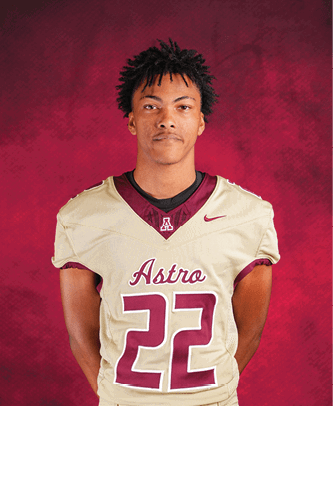 A person with short, curly hair is standing against a red background wearing a beige football jersey with the word Astro and the number 22 in maroon. Description generated by AI
