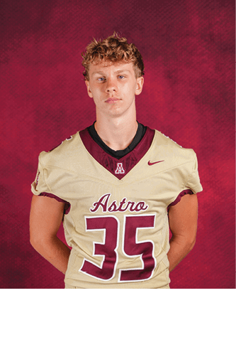 A person with curly hair wearing a beige and maroon football jersey with the number 35 and the word Astro stands against a red textured background with hands behind their back. Description generated by AI