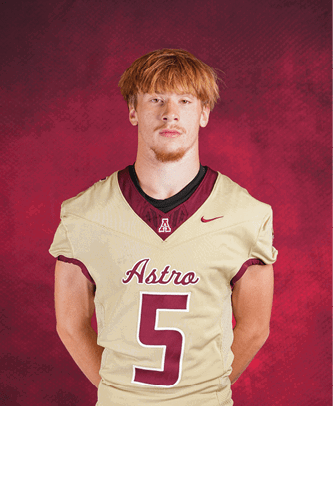 A person with short reddish hair wearing a beige football jersey with the word “Astro" and the number 5 stands against a red textured background with hands behind their back. Description generated by AI