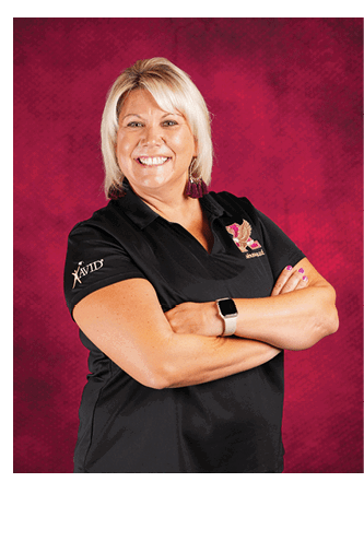 A person with short blonde hair is smiling with arms crossed, wearing a black polo shirt with logos and a smartwatch, standing against a textured red background. Description generated by AI