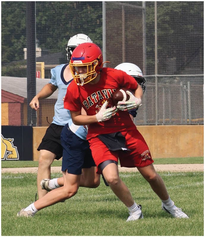 Three football players in blue and white uniforms running on a field. Description generated by AI