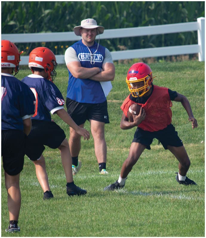Three football players in blue and white uniforms running on a field. Description generated by AI