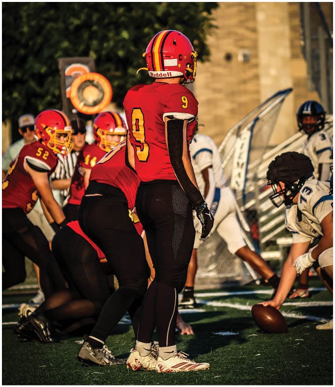Three football players in blue and white uniforms running on a field. Description generated by AI