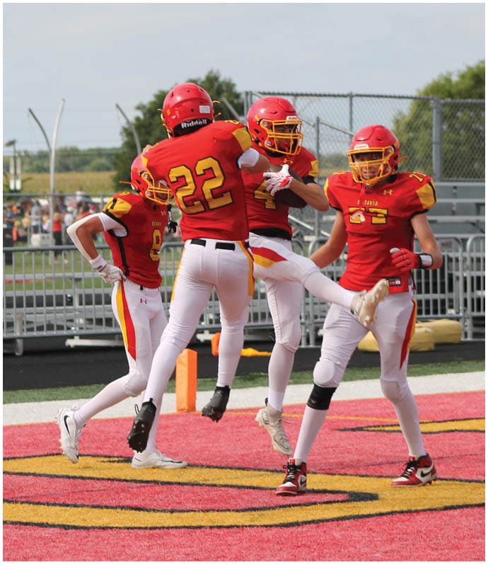 Three football players in blue and white uniforms running on a field. Description generated by AI
