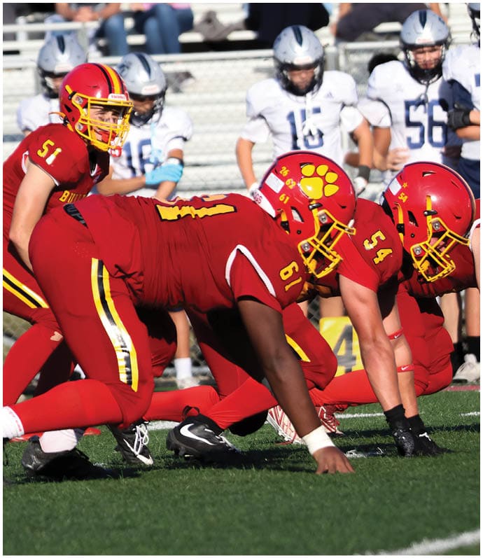 Three football players in blue and white uniforms running on a field. Description generated by AI