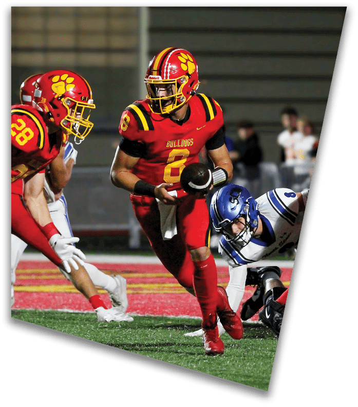 A person wearing a dark football uniform and helmet with “American Canyon" on the jersey is kneeling on one knee on a field at night. Description generated by AI