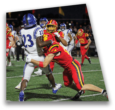 A person in football gear and helmet is crouched on a field with other players lined up in the background during a game. Description generated by AI