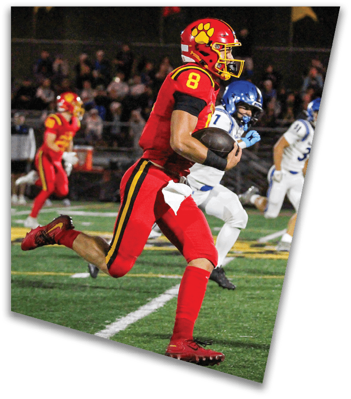 A person wearing a dark football uniform and helmet with “American Canyon" on the jersey is kneeling on one knee on a field at night. Description generated by AI
