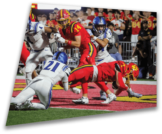 Four people in dark football uniforms and helmets stand in a row on a field, appearing focused and ready for action. Description generated by AI