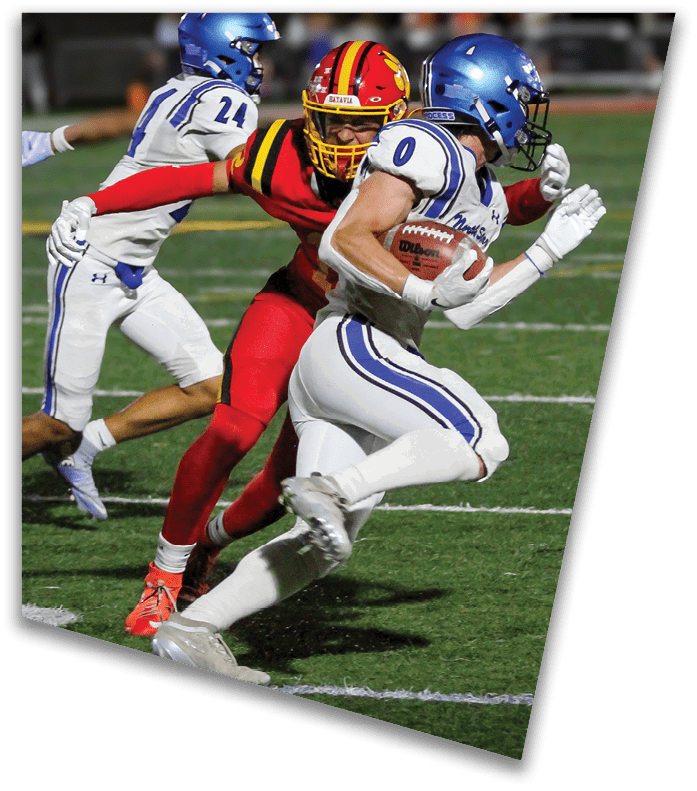 A person wearing a dark football uniform and helmet with “American Canyon" on the jersey is kneeling on one knee on a field at night. Description generated by AI
