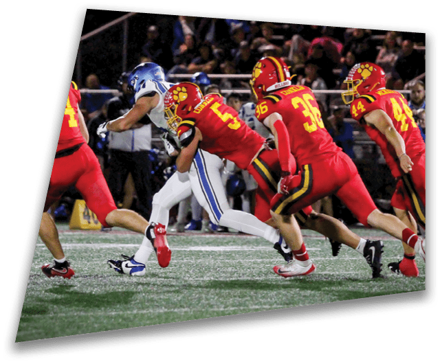 Four people in dark football uniforms and helmets stand in a row on a field, appearing focused and ready for action. Description generated by AI